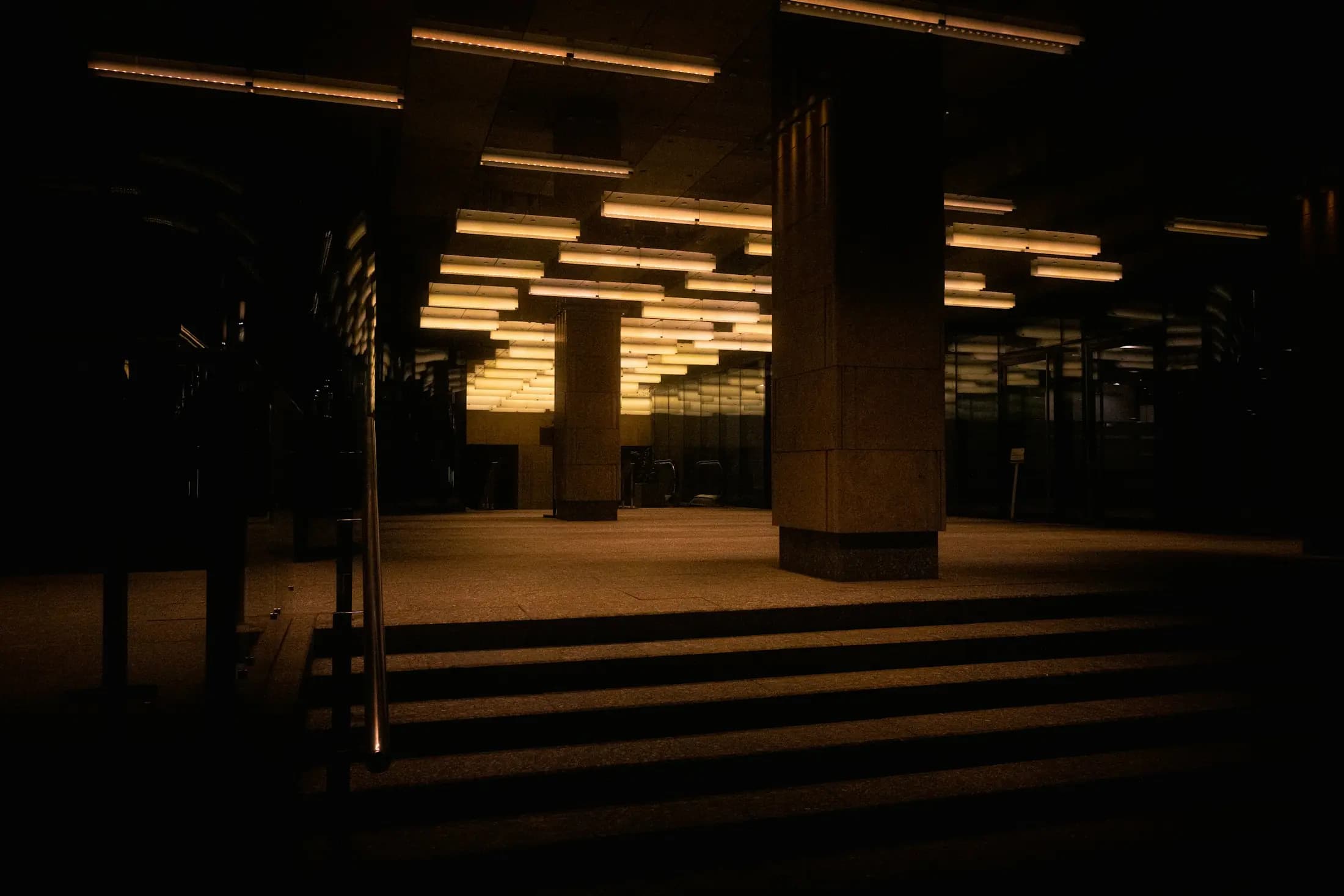 Un escalier dans un hall sombre, sous des rangées de lumière